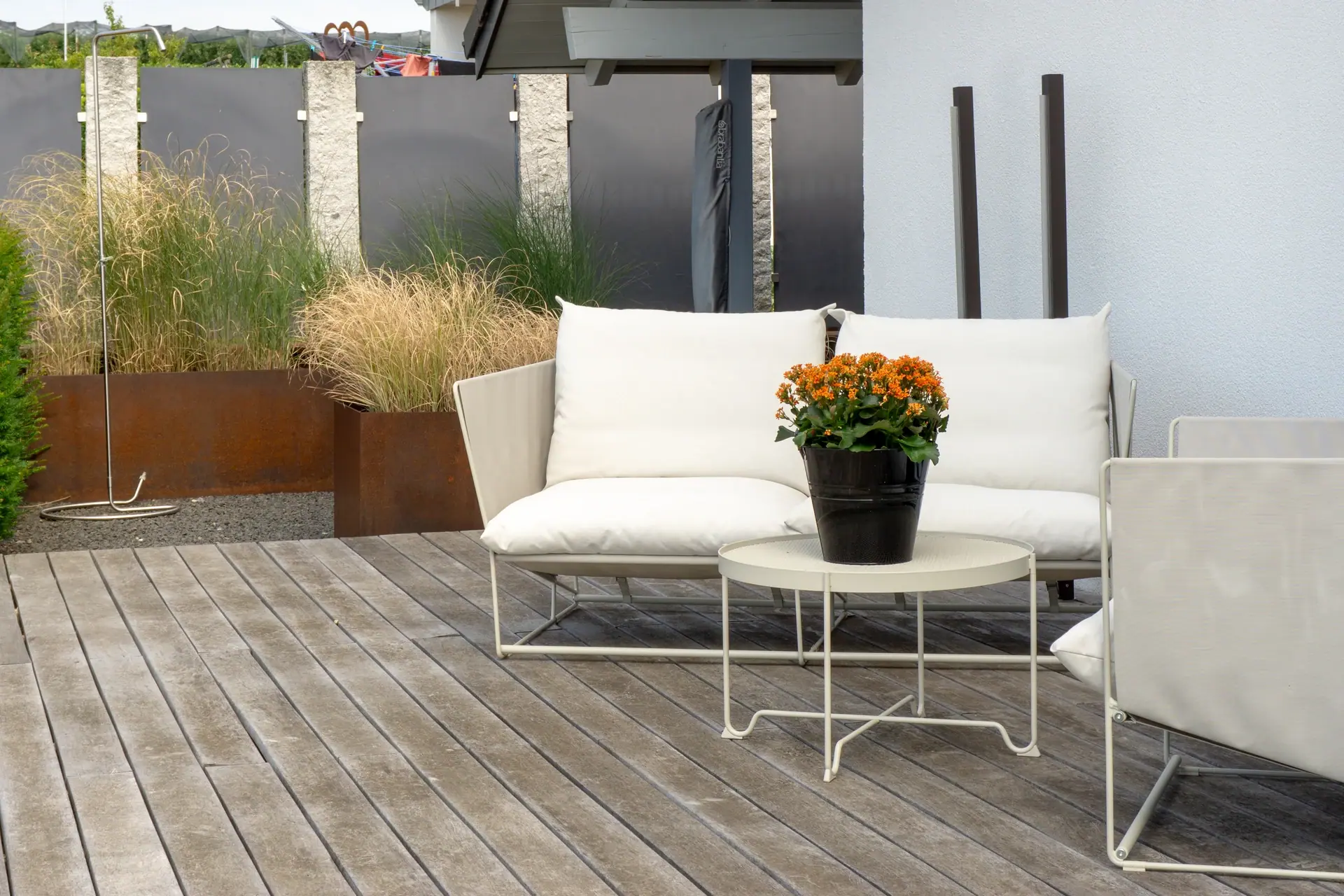 Helles Sofa mit Blumenschale auf einer Holzterrasse.