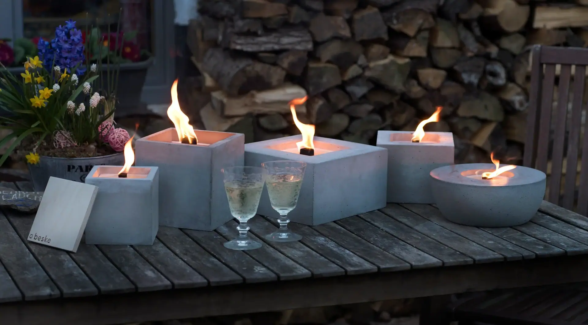 Mehrere kleine Tischfeuer auf einem Holztisch im Garten.