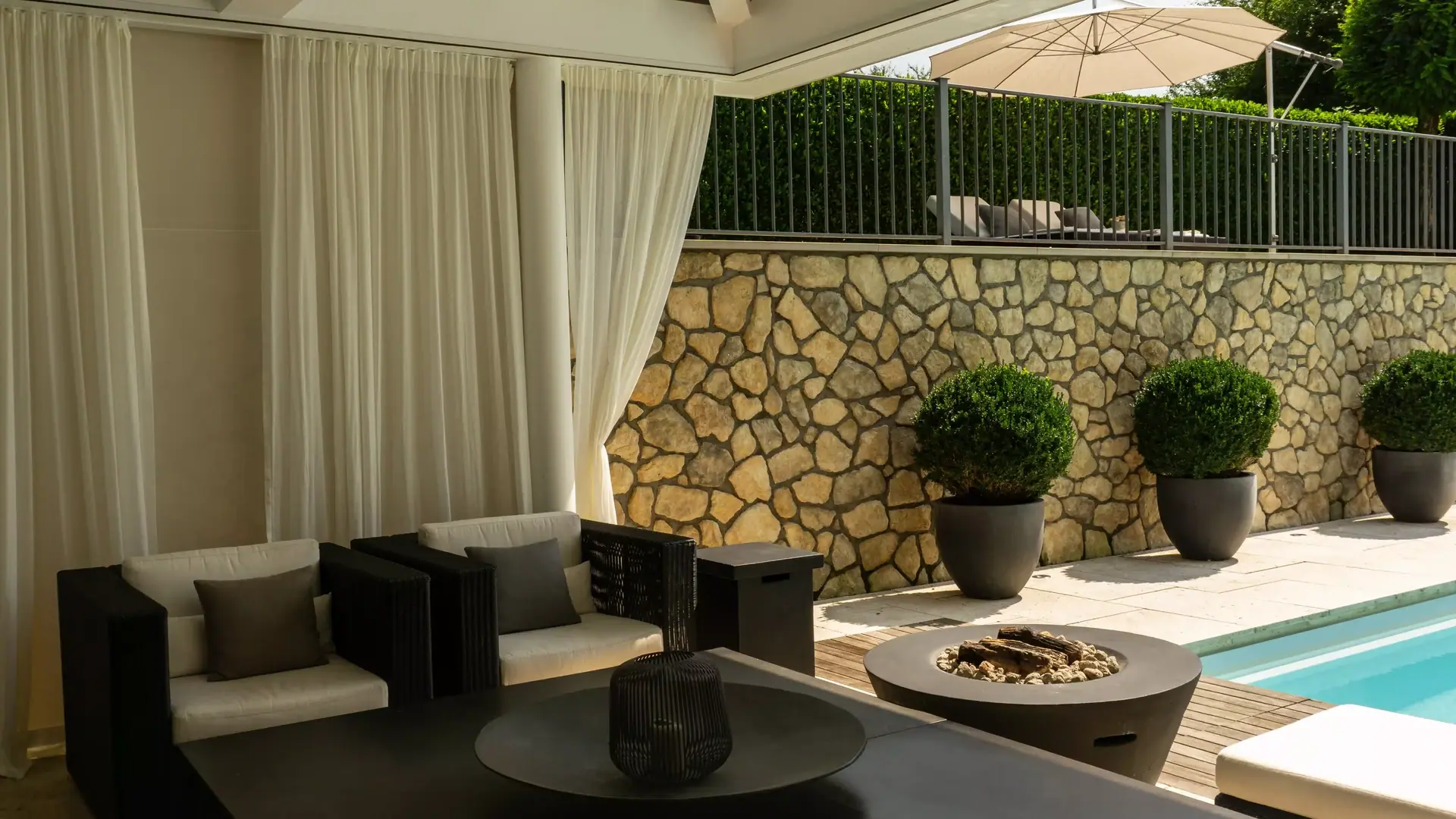 Überdachte Gartenlounge mit Sitzmöbeln neben einem Pool.