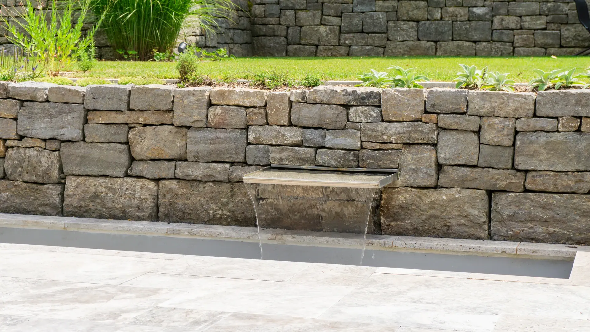Wasserauslauf aus einer Natursteinmauer auf einer Terrasse.