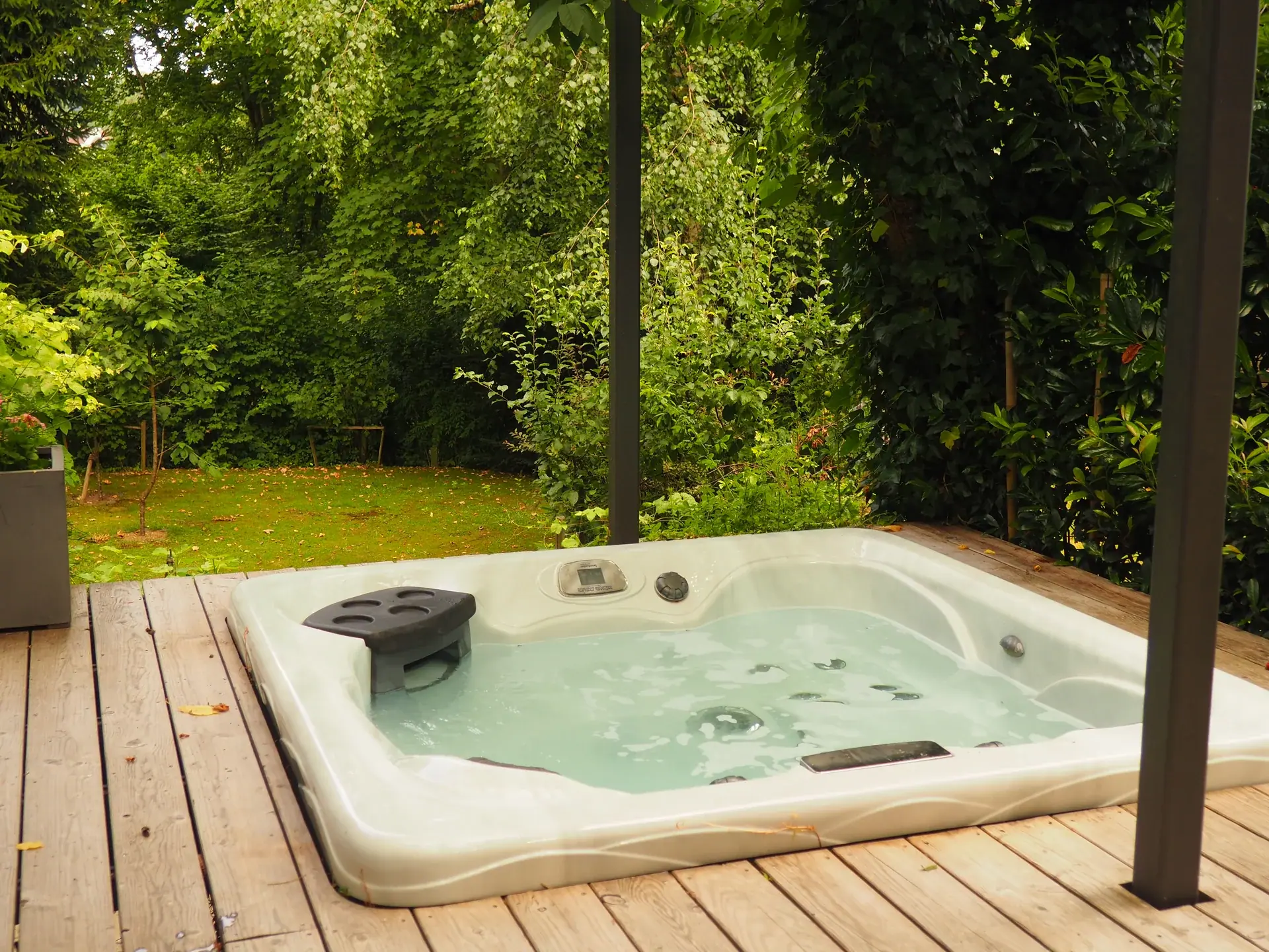 Whirlpool auf einem Holzdeck neben grünen Bäumen.