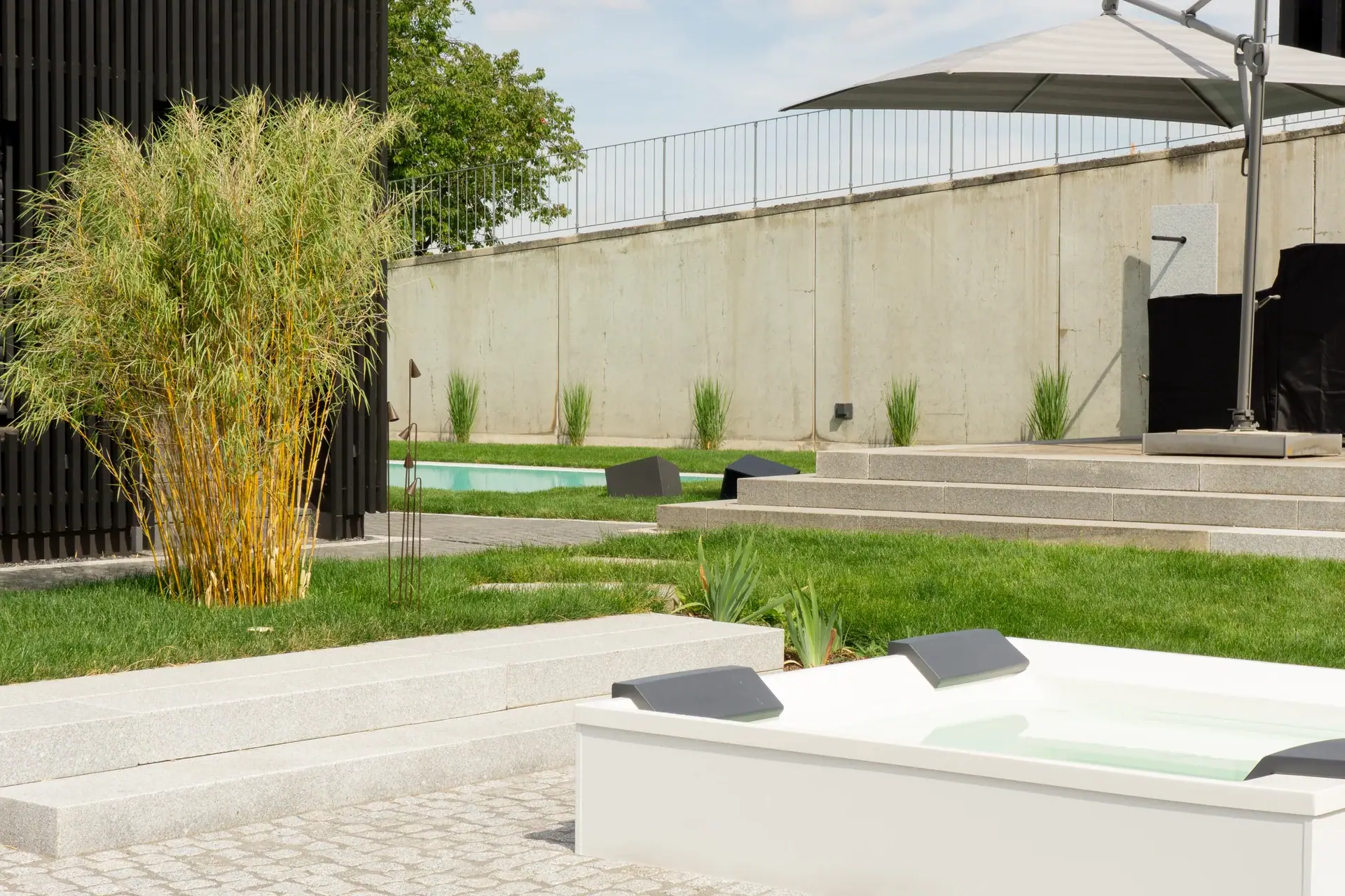 Whirlpool auf einer Terrasse mit Ziergräsern und Mauern.