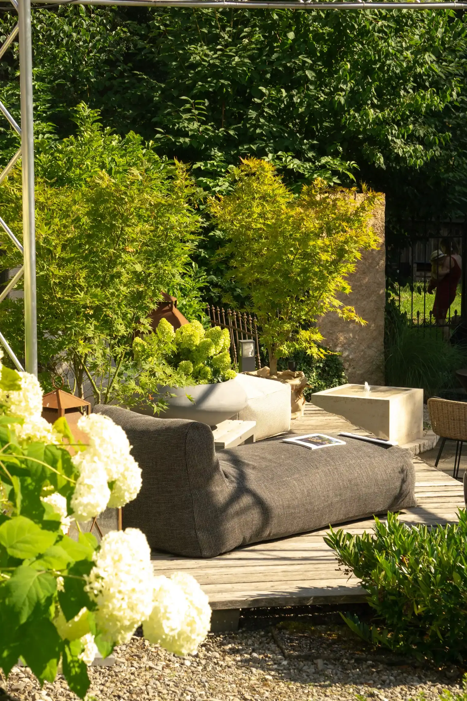Ausstellungsgarten von WohnraumGarten mit Lounge-Möbeln auf einer Holzterrasse, umgeben von Hortensien und Ahorn
