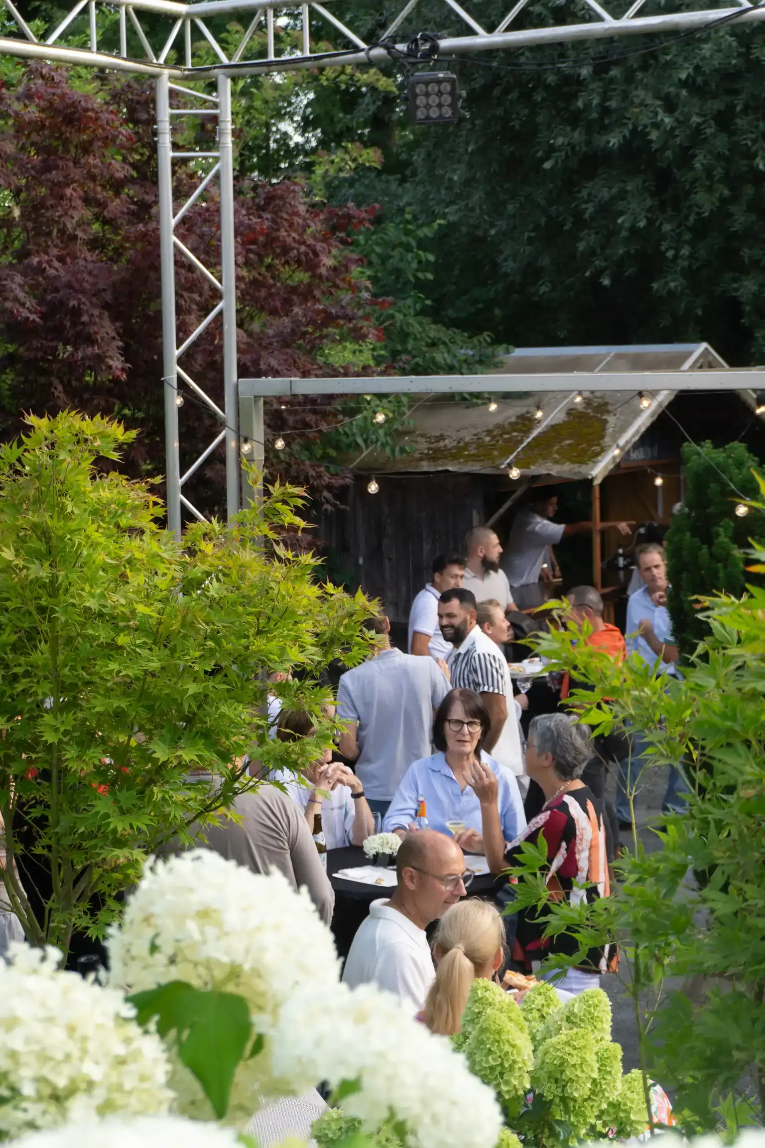 Gäste an Stehtischen zwischen Hortensien und Lichterketten auf dem Festgelände von WohnraumGarten