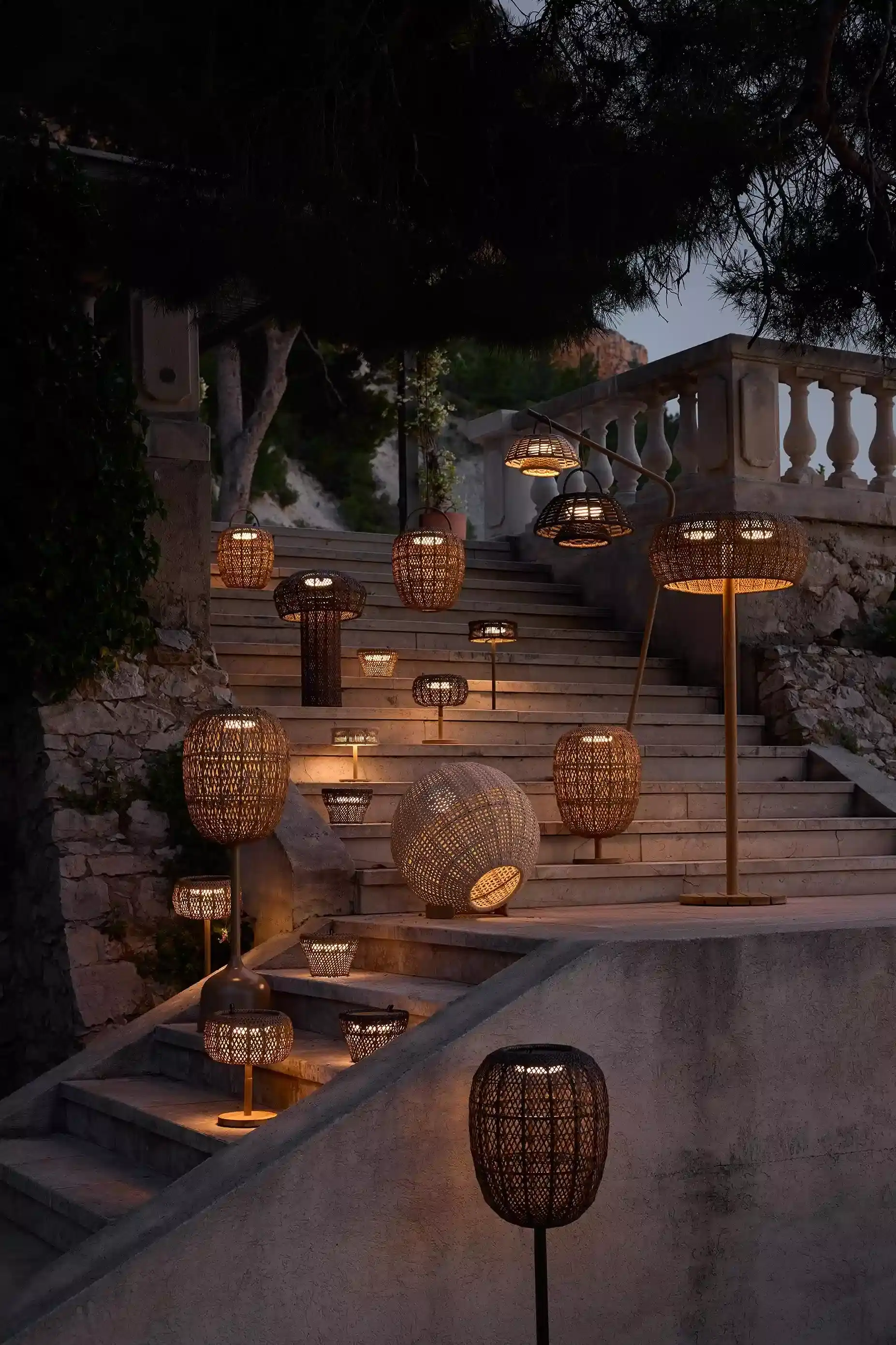 Outdoor-Leuchten aus Rattan leuchten abends auf einer Steintreppe und schaffen warmes Licht im Garten.