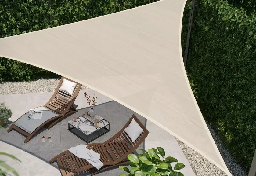 Beiges dreieckiges Sonnensegel über zwei Holz-Sonnenliegen und einem Couchtisch auf einer Terrasse.